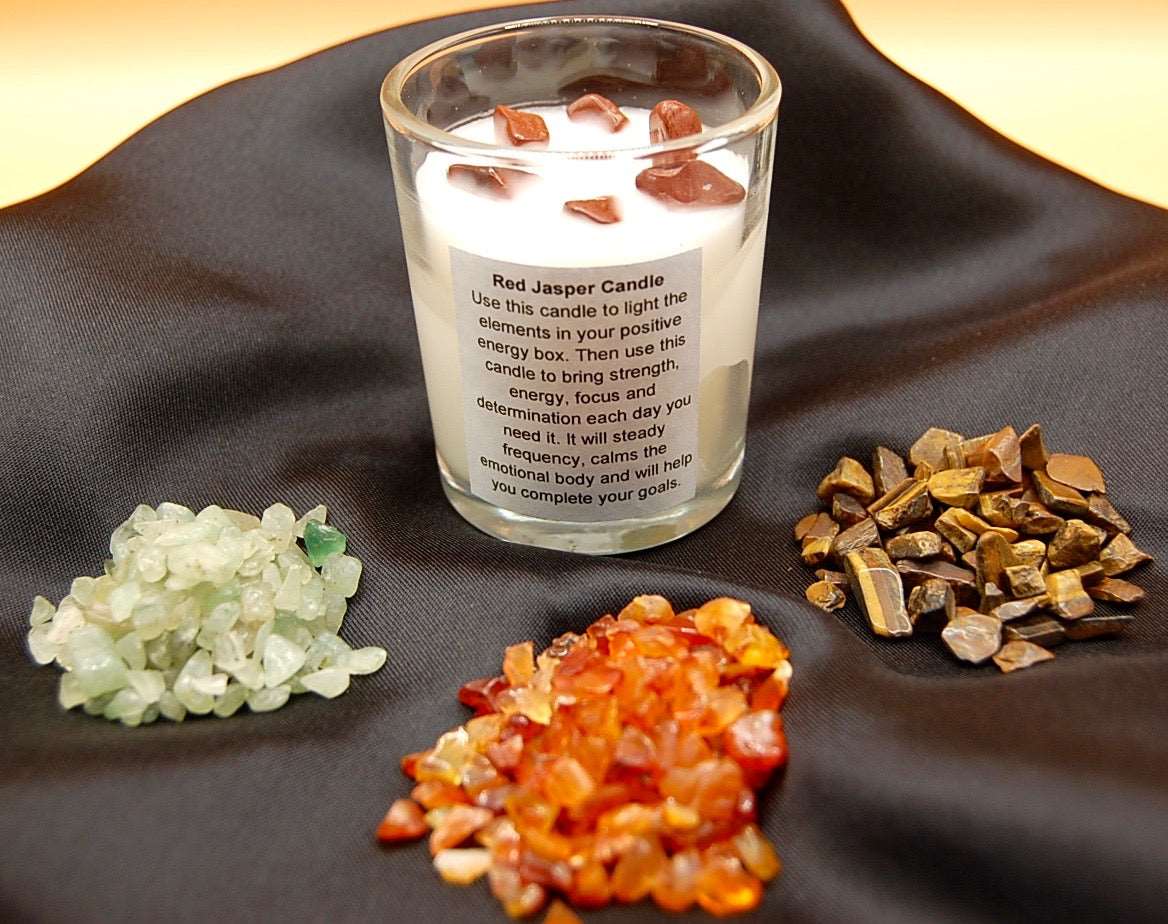 candle with red jasper crystals and 3 small piles of other crystals on a black silk napkin